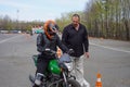 A young woman is learning to ride a motorbike in a motorcycle school. She is taught by a teacher