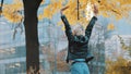 Young woman in leather jacked jumps from excitement under the autumn colored tree in the city park Royalty Free Stock Photo