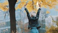 Young woman in leather jacked jumps from excitement under the autumn colored tree in the city park Royalty Free Stock Photo