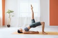 Young woman in leggings and short T-shirt, practicing yoga, doing dvipada pithasana with leg extended upward, half bridge pose Royalty Free Stock Photo