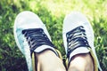 Young Woman Legs In Pair Of Sport Shoes Sneakers  Of Blue Suede On The Grass Lawn In Park