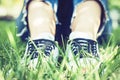 Young Woman Legs In Pair Of Sport Shoes Sneakers  Of Blue Suede On The Grass Lawn In Park