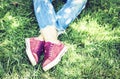 Young woman legs in sport shoes sneakers of pink suede, sitting on the grass lawn in park Royalty Free Stock Photo