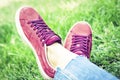 Young woman legs in sport shoes sneakers of pink suede, sitting on the grass lawn in park Royalty Free Stock Photo