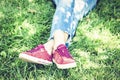 Young woman legs in sport shoes sneakers of pink suede, sitting on the grass lawn in park Royalty Free Stock Photo