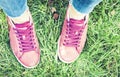 Young Woman Legs In Sport Shoes Sneakers Of Pink Suede, Standing On The Grass Lawn In Park