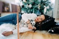 Woman lies on the floor near Christmas tree and plays with puppy of dalmatian dog