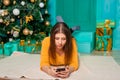 A young woman lies on a fur carpet with a smartphone in her hands on the background of a Christmas tree Royalty Free Stock Photo