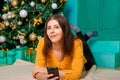 A young woman lies on a fur carpet with a smartphone in her hands on the background of a Christmas tree Royalty Free Stock Photo