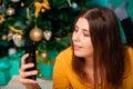 A young woman lies on a fur carpet with a smartphone in her hands on the background of a Christmas tree Royalty Free Stock Photo