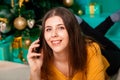 A young woman lies on a fur carpet with a smartphone in her hands on the background of a Christmas tree Royalty Free Stock Photo