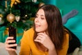 A young woman lies on a fur carpet with a smartphone in her hands on the background of a Christmas tree Royalty Free Stock Photo