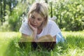 A young woman lies on the grass in the park and reads a book. Pretty blonde with freckles. Rest on a sunny summer day Royalty Free Stock Photo