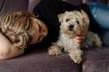 Young woman lies on pink sofa and hugs Yorkshire Terrier dog. They are happy and relaxed together. Dog looks at camera. Concept of Royalty Free Stock Photo