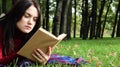 A young woman lies and reads her favorite book on a woolen plaid blanket or blanket in a city park on green grass on a pleasant Royalty Free Stock Photo