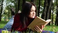 A young woman lies and reads her favorite book on a woolen plaid blanket or blanket in a city park on green grass on a pleasant Royalty Free Stock Photo