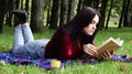 A young woman lies and reads her favorite book on a woolen plaid blanket or blanket in a city park on green grass on a pleasant Royalty Free Stock Photo