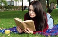 A young woman lies and reads her favorite book on a woolen plaid blanket or blanket in a city park on green grass on a pleasant Royalty Free Stock Photo