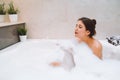 Young woman lies in white bath of foam with her eyes closed. Spa procedures, cleansing, relaxation, self-care. Royalty Free Stock Photo