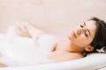Young woman lies in white bath of foam with her eyes closed. Spa procedures, cleansing, relaxation, self-care. Royalty Free Stock Photo