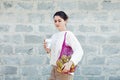 Young woman in light clothes with eco bag with apples and reusable coffee mug. Background gray brick wall. Sustainable lifestyle.