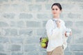Young woman in light clothes with eco bag with apples and reusable coffee mug. Background gray brick wall. Sustainable lifestyle.