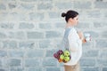 Young woman in light clothes with eco bag with apples and reusable coffee mug. Background gray brick wall. Sustainable lifestyle.