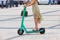 A girl in a light dress rides an electric scooter along a cobbled city square. The concept of eco-friendly free movement