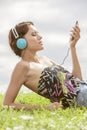 Young woman listening to music through MP3 player using headphones while lying on grass against sky Royalty Free Stock Photo