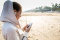 Young woman is listening to the music on the phone before jogging on the beach at the sunrise