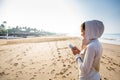 Young woman is listening to the music on the phone before jogging on the beach at the sunrise