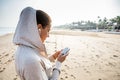Young woman is listening to the music on the phone before jogging on the beach at the sunrise