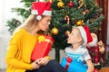 Happy mom and son wearing santa hat sharing presents under tree Royalty Free Stock Photo