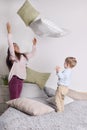 Young woman, little son throw pillows on grey bed