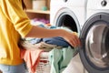 Young woman loading colorful laundry into washing machine