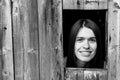 A young woman locked in a wooden shed, peeking through a small window.