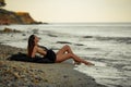 Young woman in long black dress sits on sand beach by the sea. Royalty Free Stock Photo