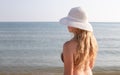 A young woman with long blond hair in a swimsuit and a white hat with large brim on the seashore. Sea travel and leisure