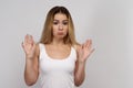 Young woman with long blond hair in white tank top stands on isolated background. Beautiful girl shows that she is not guilty Royalty Free Stock Photo