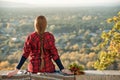 Young woman with long braid sits on a hill overlooking the village. Back view