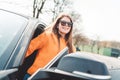 Young woman with long brown hair and big smile on her face stepping out of a black car on a sunny day Royalty Free Stock Photo