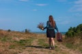 Woman with long brown hair in denim jacket, black skirt, vintage suitcase, flowers bouquet off-road. Lifestyle photo Royalty Free Stock Photo