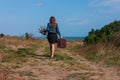 Woman with long brown hair in denim jacket, black skirt, vintage suitcase, flowers bouquet off-road. Lifestyle photo Royalty Free Stock Photo