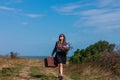 Woman with long brown hair in denim jacket, black skirt, vintage suitcase, flowers bouquet off-road. Lifestyle photo Royalty Free Stock Photo