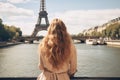 Young woman with long curly hair looking at Eiffel tower in Paris, France, Young traveler woman rear view sitting on the quay of