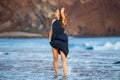 Young woman in long dark blue dress walking through waves on the beach Royalty Free Stock Photo