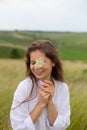 Closeup portrait of a young woman with long dark hair standing in a field smiling with closed eyes with a flower in her hands Royalty Free Stock Photo