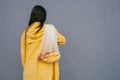 Woman with long dark hair wearing yellow raincoat holding string shopper bag with fruits standing back to the camera against Royalty Free Stock Photo