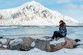 A young woman with long hair admiring the winter view of the fjord, sits on a rock near the water. On the background a large snowy Royalty Free Stock Photo