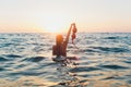 Young woman with long hair, blonde, topless, sitting in the water and holding in his hand a bikini top in the sunshine. Royalty Free Stock Photo